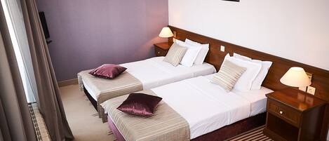 A hotel room with two beds, a nightstand with a lamp, a wall-mounted picture, and a radiator.