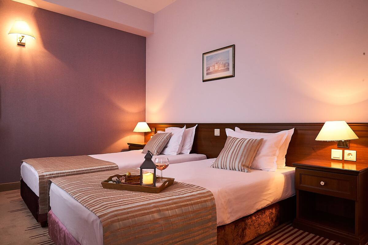 A hotel room with two beds, a nightstand with a lamp, a tray with a candle, and a framed picture on the wall.