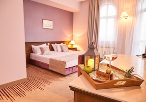 A hotel room with a neatly made bed, a bedside table with a tray of snacks, a wine glass, and a lantern.