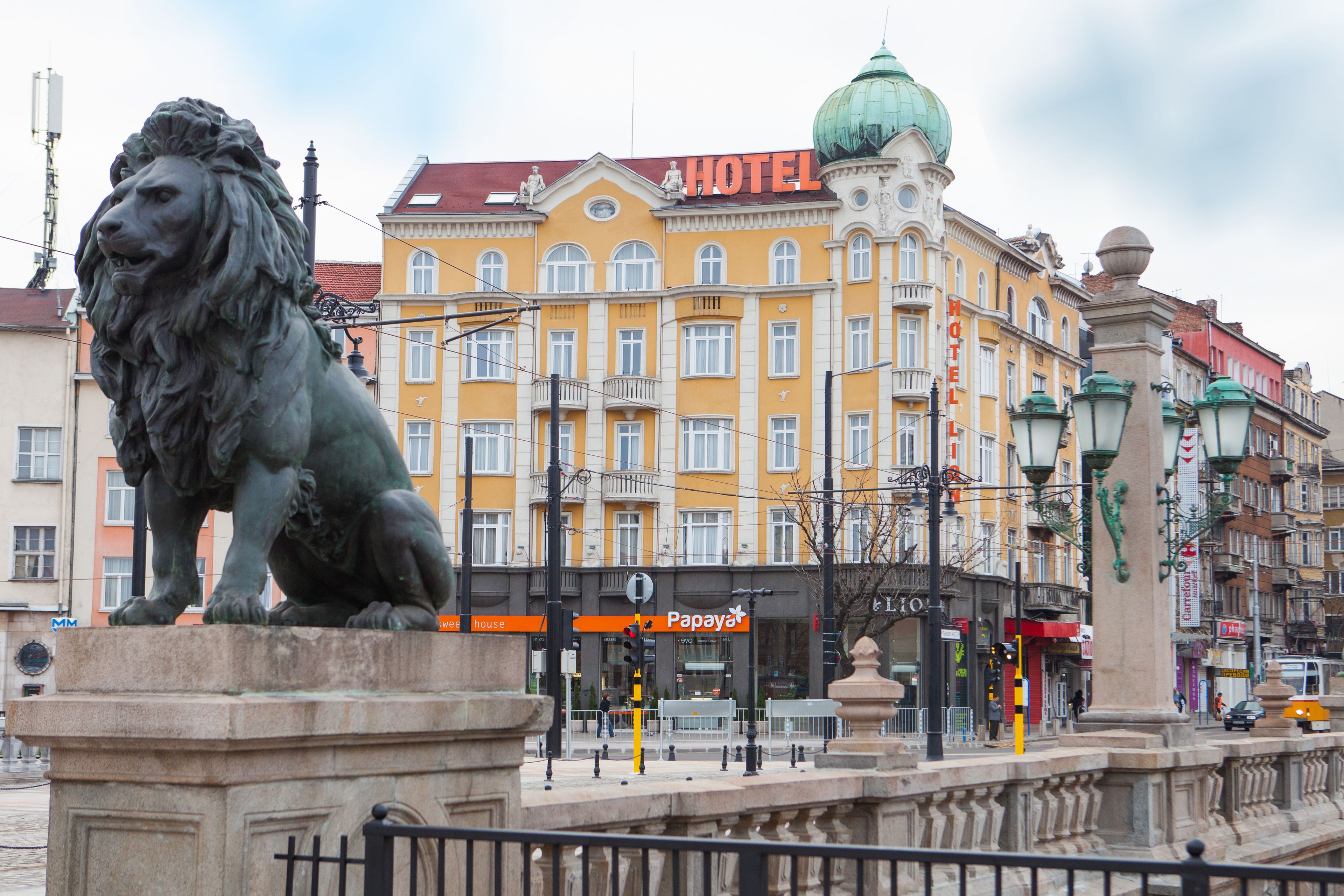 A hotel with a yellow facade, a lion statue in front, and a dome on the building.