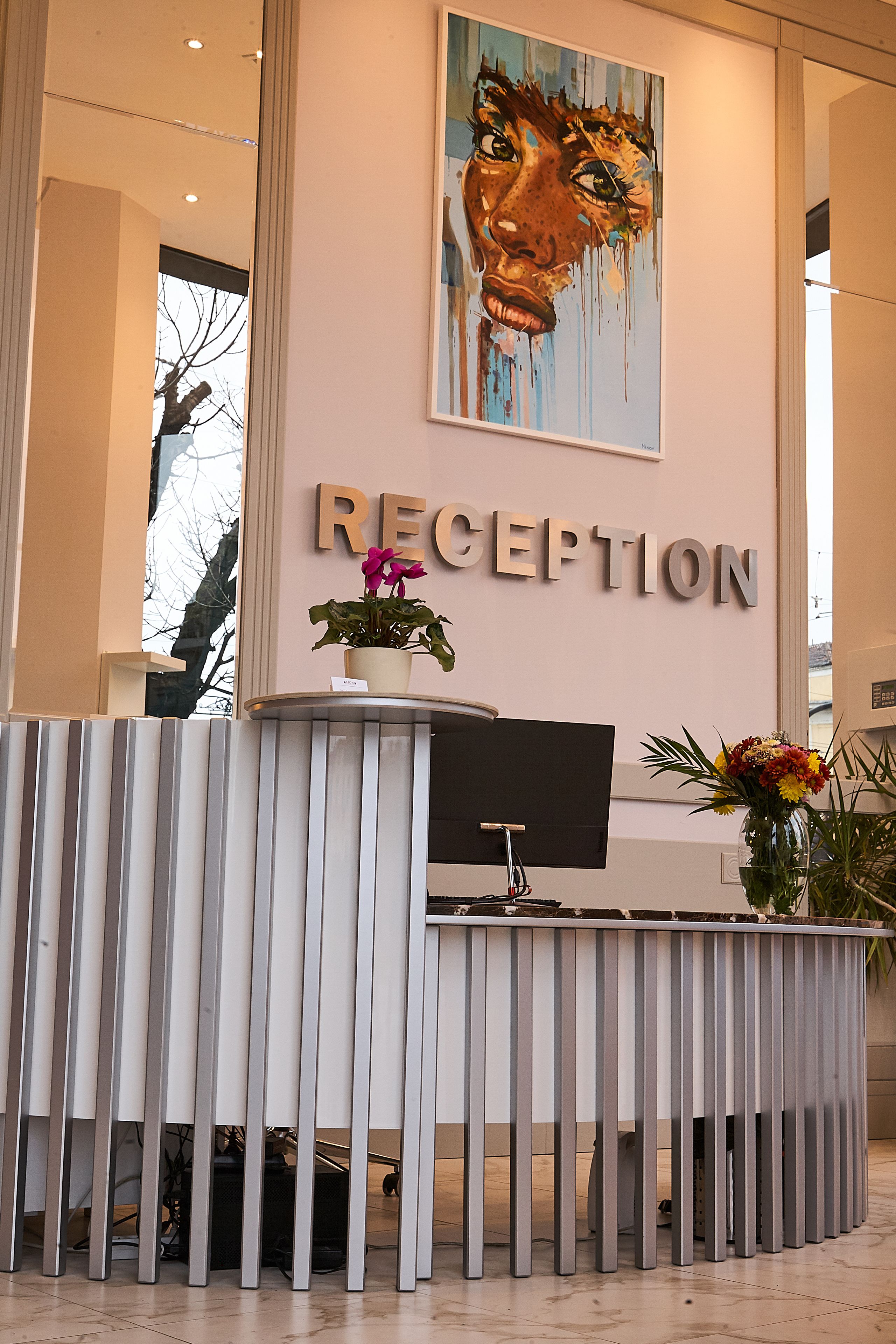 Een receptiebalie met een bordje met daarop 'RECEPTION', een potplant en een vaas met bloemen.