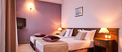 Habitación de hotel con dos camas, televisión, mesita de noche con lámpara y un cuadro en la pared.