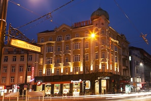 A hotel with a prominent dome and multiple balconies, surrounded by other buildings and street lights.