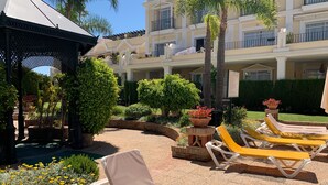 Une cour d’hôtel aménagée avec des chaises longues, une pergola et des espaces verts bien entretenus.
