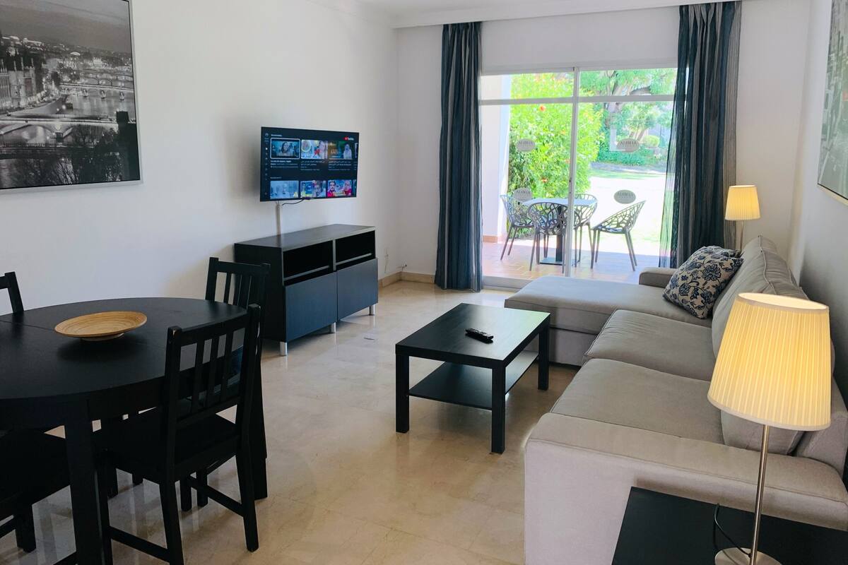 Een moderne woonkamer met een flatscreen televisie, een eettafel, een bank en een lamp.