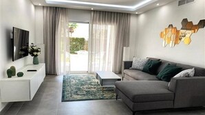 Un salon moderne avec un canapé gris, un buffet blanc, un téléviseur à écran plat et un élément décoratif mural.