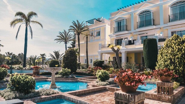 Un complexe hôtelier doté d’une piscine entourée de palmiers et de jardins bien entretenus.