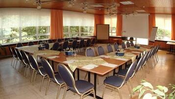 A conference room with a long table, chairs, a projector screen, and windows with curtains.