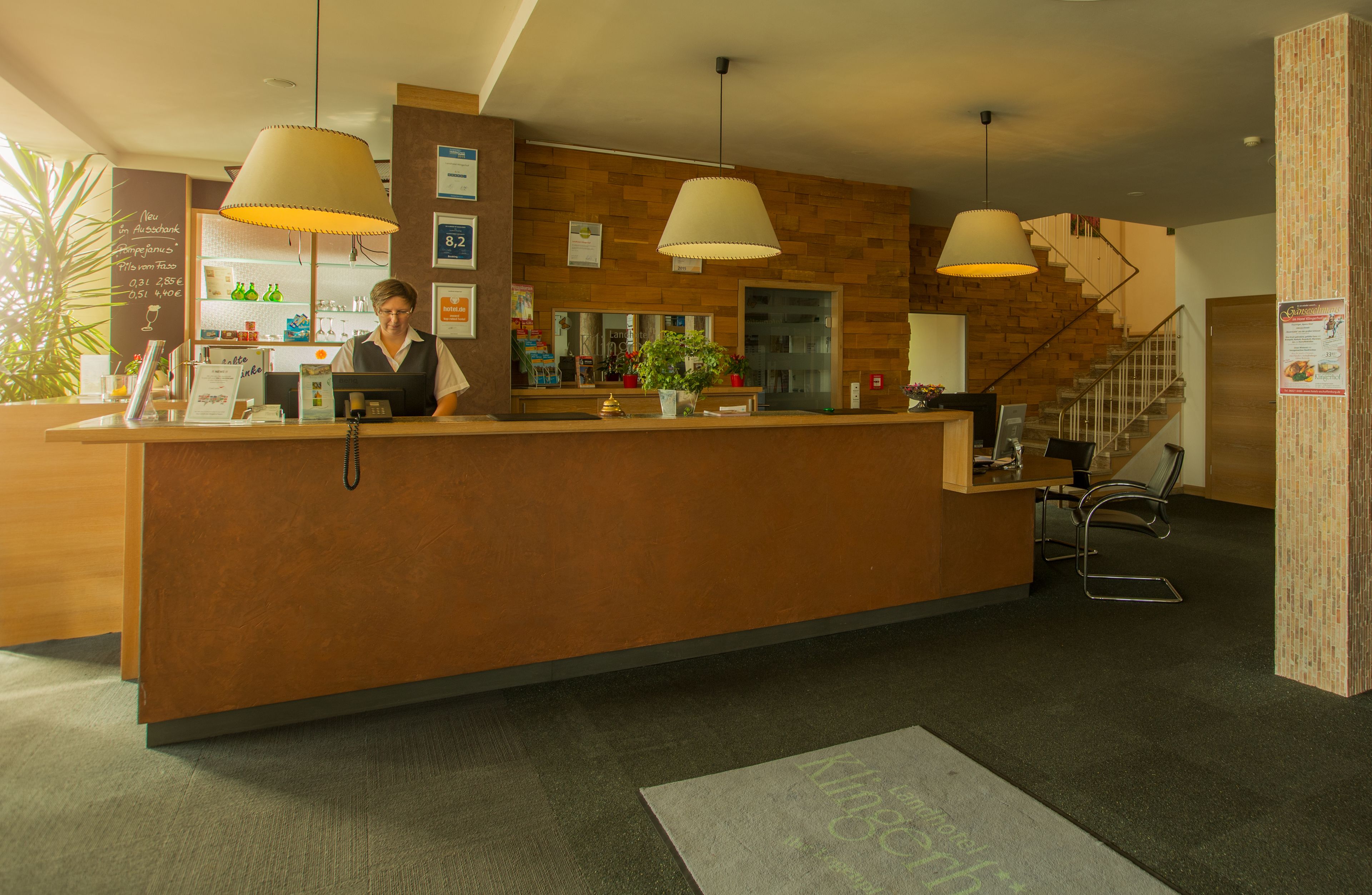 A reception desk with a wooden counter, two pendant lights, a plant, and a staircase in the background.