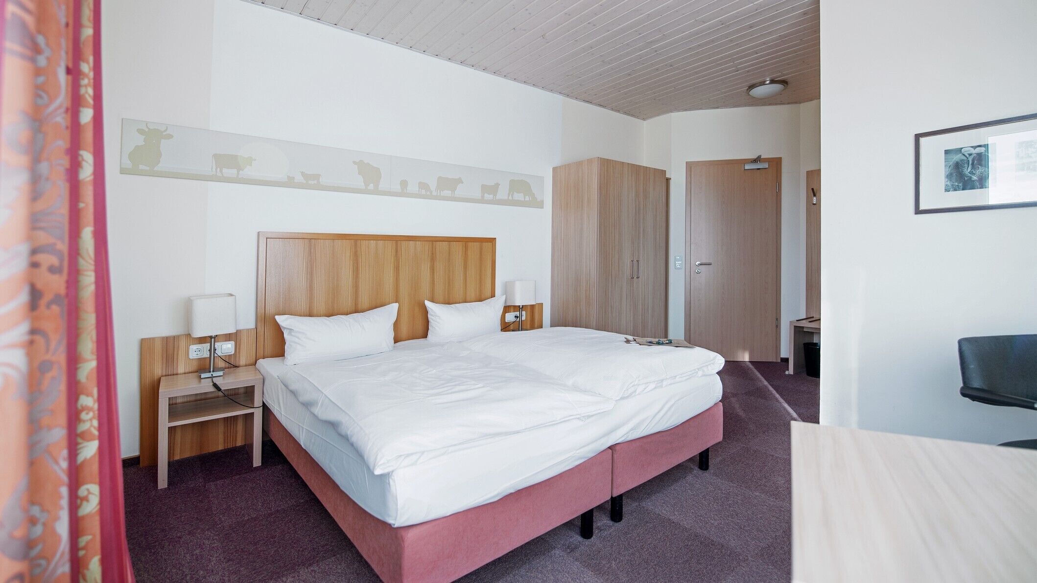 Habitación de hotel con una cama grande, cabecera de madera, mesitas de noche con lámparas, un armario y un escritorio con silla.