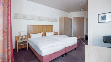 Habitación de hotel con una cama grande, cabecera de madera, mesitas de noche con lámparas, un armario y un escritorio con silla.