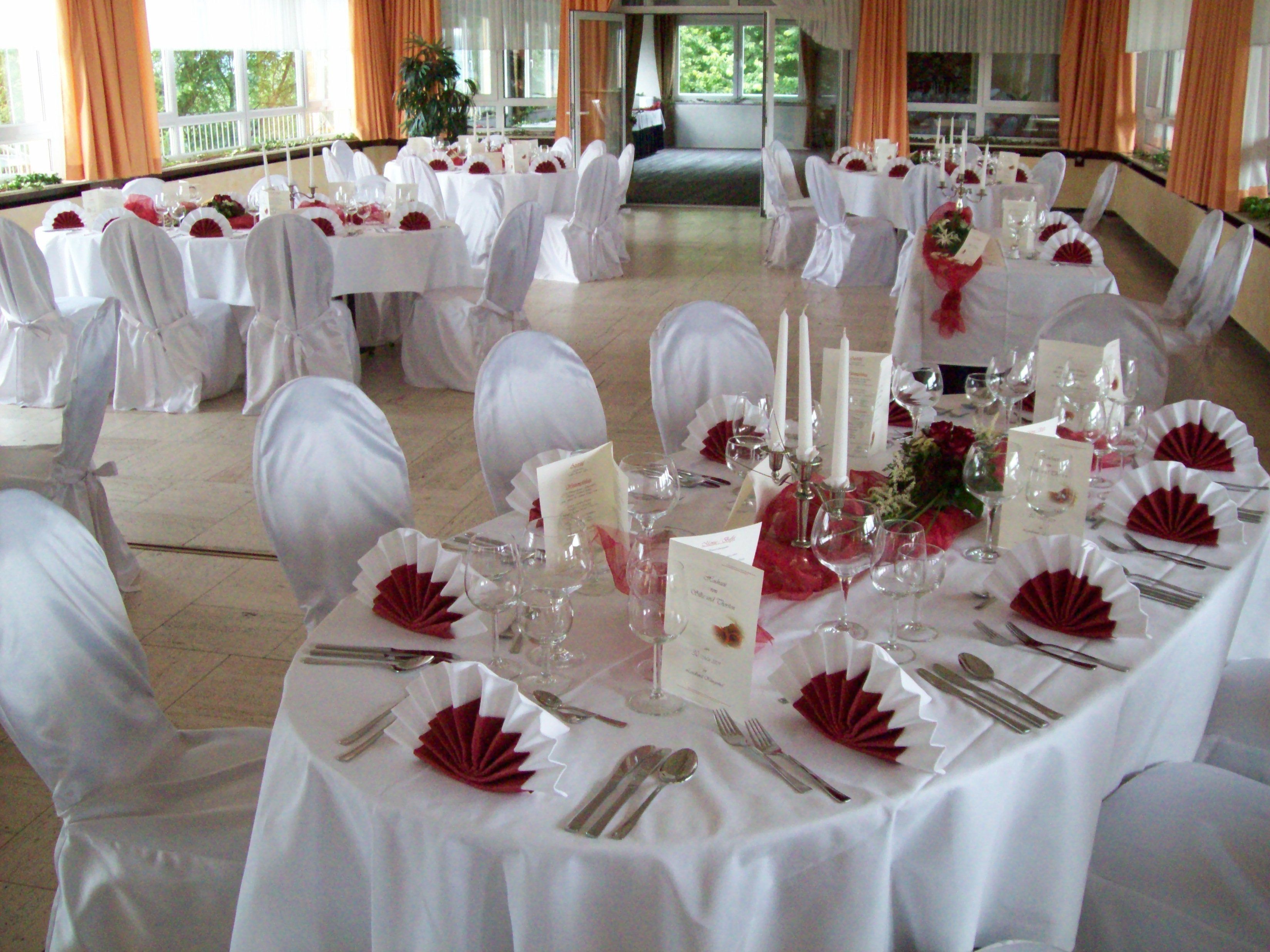 Un salón de banquetes con mesas redondas dispuestas para un evento formal, con manteles blancos, servilletas dobladas y cubiertos.