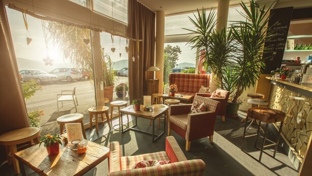A cozy cafe with a mix of seating options, including a sofa and chairs, a bar area, and a view of parked cars outside.