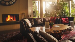 A cozy living room with a fireplace, leather sofas, a coffee table, and a view of greenery outside.