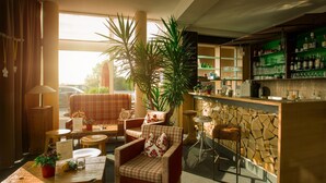 A cozy bar area with wooden furniture, a stone wall, and a variety of bottles and glasses on shelves.