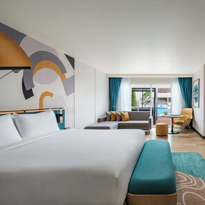 Een moderne hotelkamer met een groot bed, een bank, een klein tafeltje en uitzicht op een zwembad.