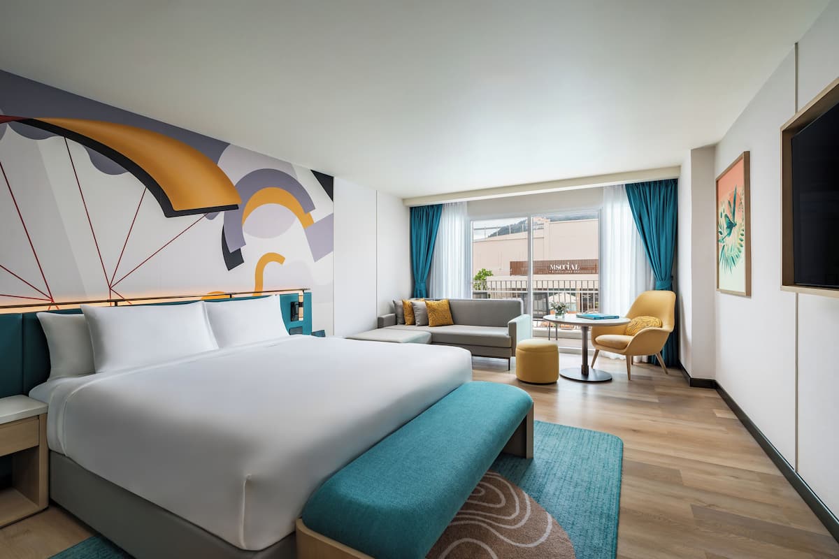 A modern hotel room with a large bed, a sofa, a small table, and a chair.