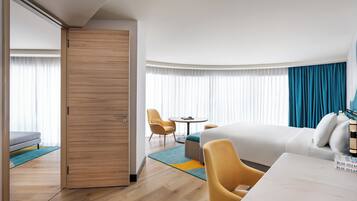 Una habitación de hotel con cama, escritorio, silla, sofá, mesa y un gran ventanal con cortinas.