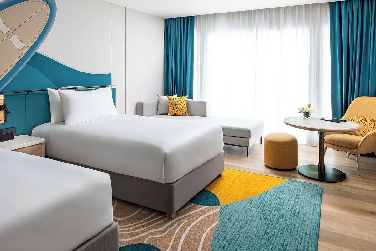 A modern hotel room with a large bed, a sofa, a small table, and a chair.