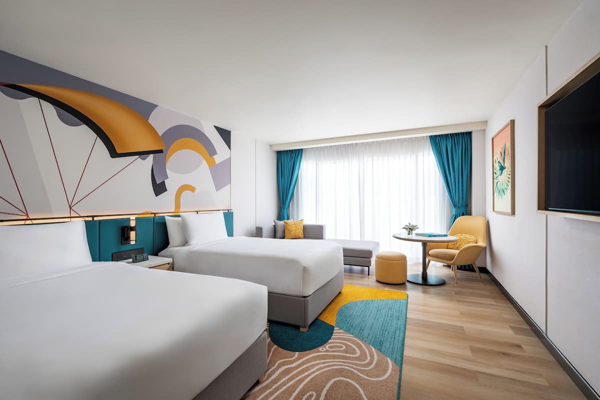 A modern hotel room with two beds, a sofa, a small table, and a TV.