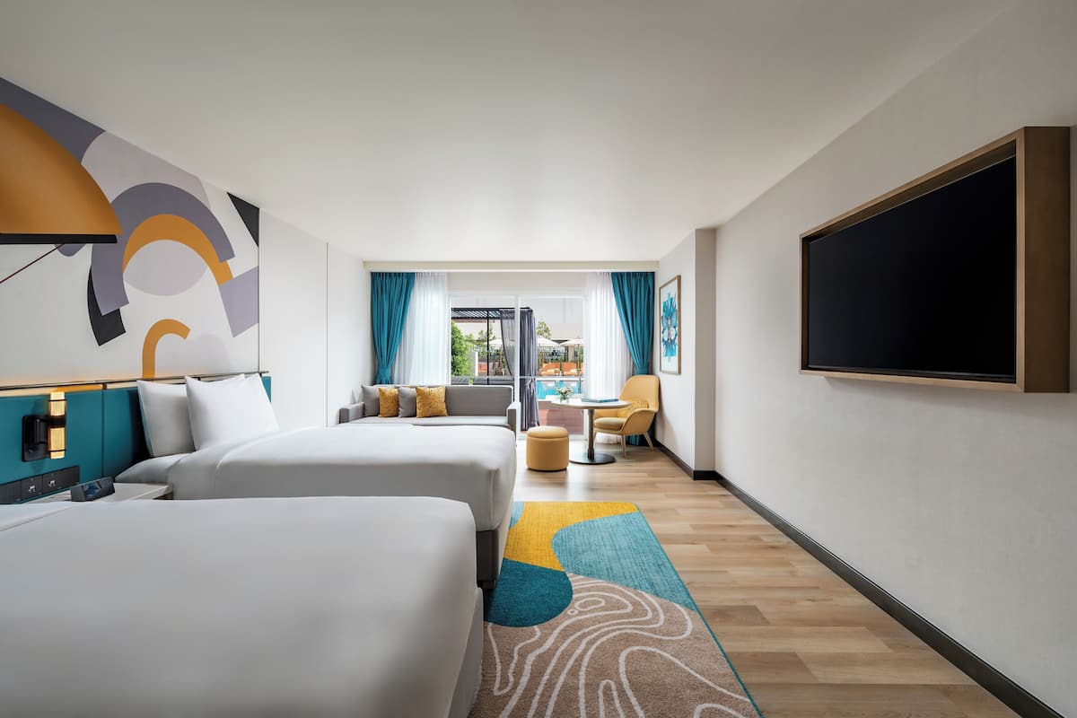 A hotel room with two beds, a TV, a sofa, a small table, and a view of the outdoors.