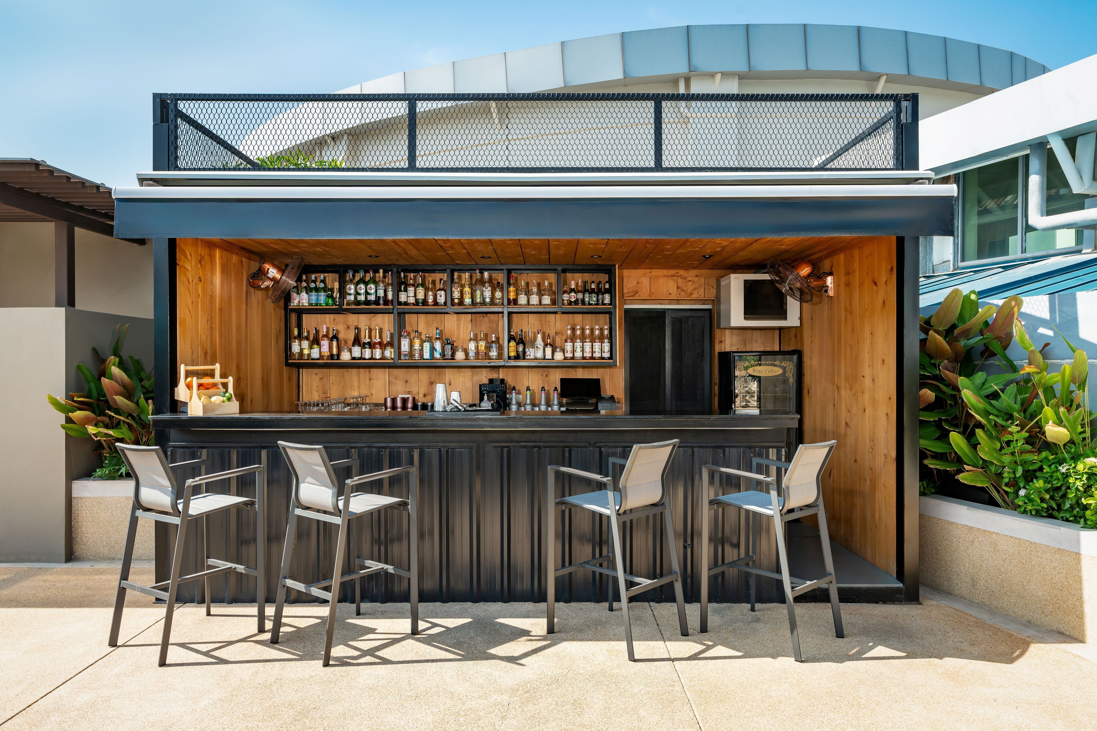 Un bar extérieur moderne doté d’un comptoir en bois, de tabourets et d’une variété de bouteilles.