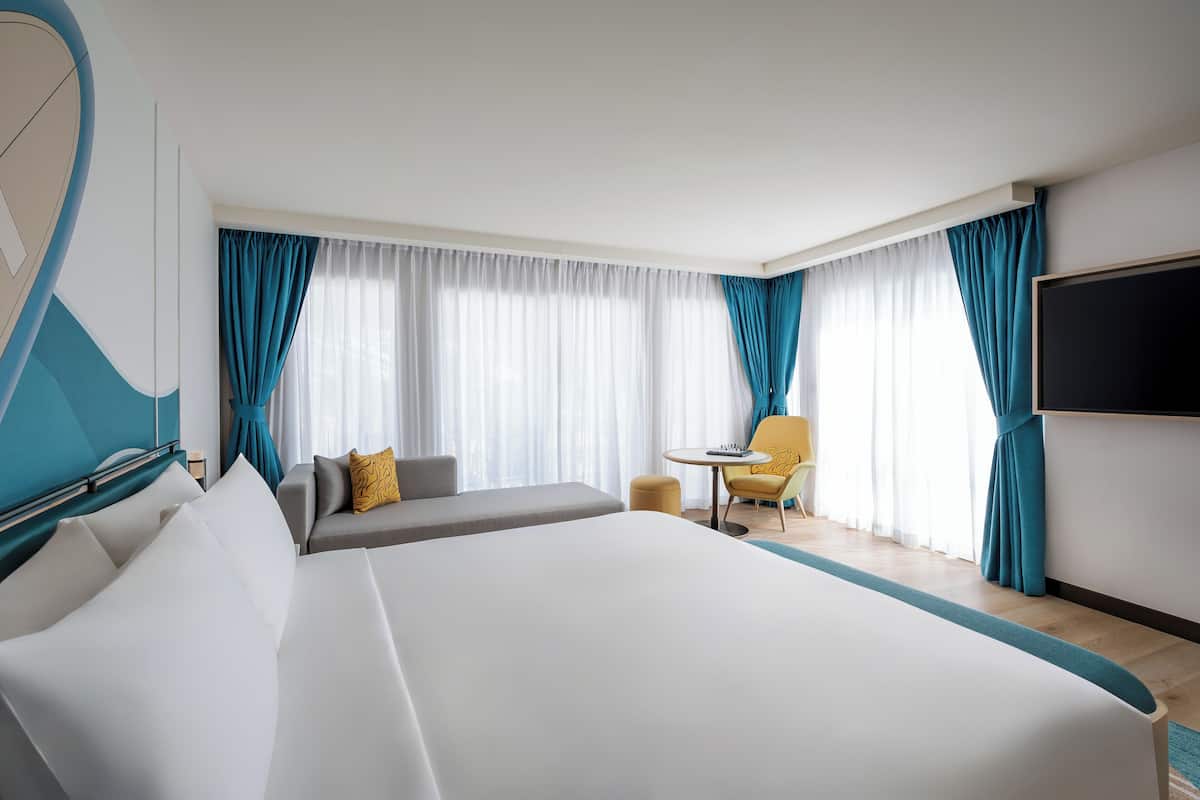 A hotel room with a large bed, a sofa, a small table, and a TV.