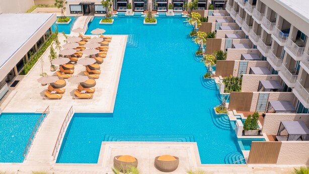Une grande piscine entourée de balcons d’hôtel, avec des chaises longues et des parasols.