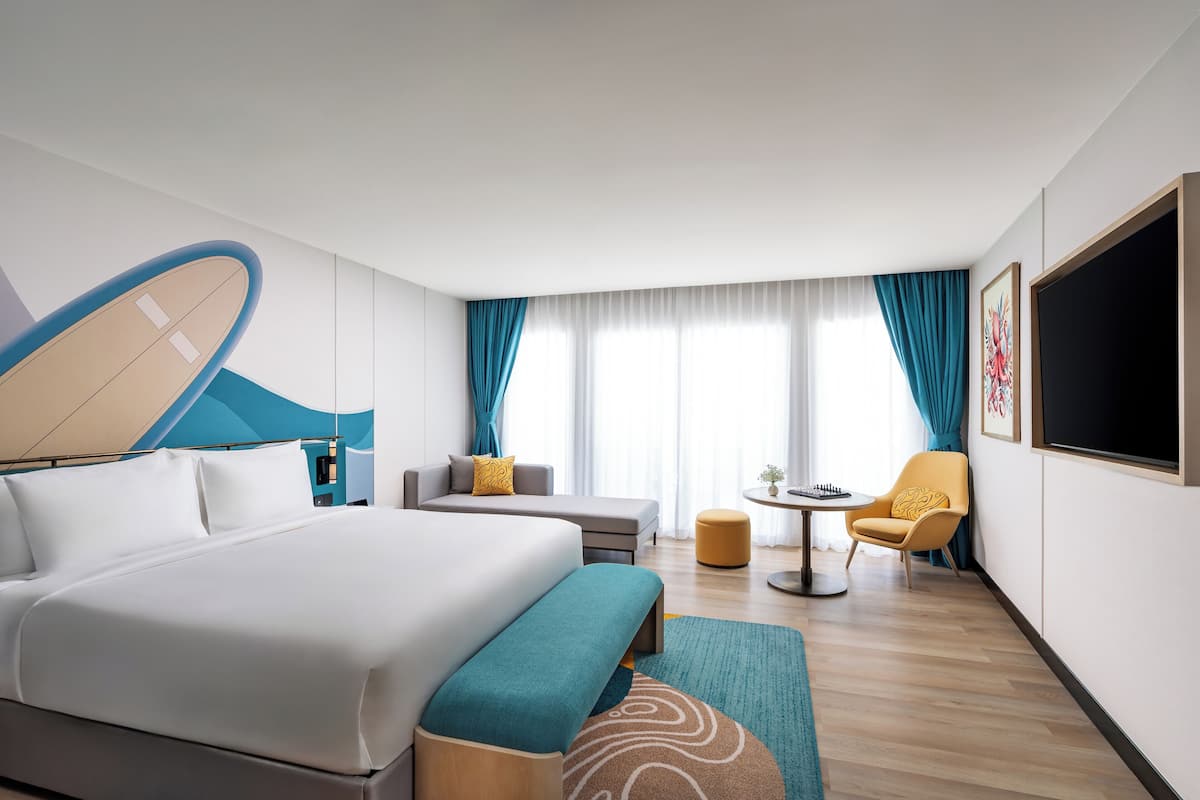 A modern hotel room with a large bed, a sofa, a small table, and a TV.