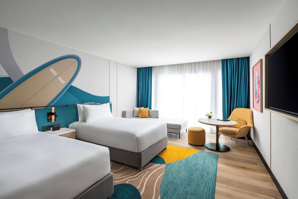 Een hotelkamer met twee bedden, een bank, een eettafeltje en een televisie.