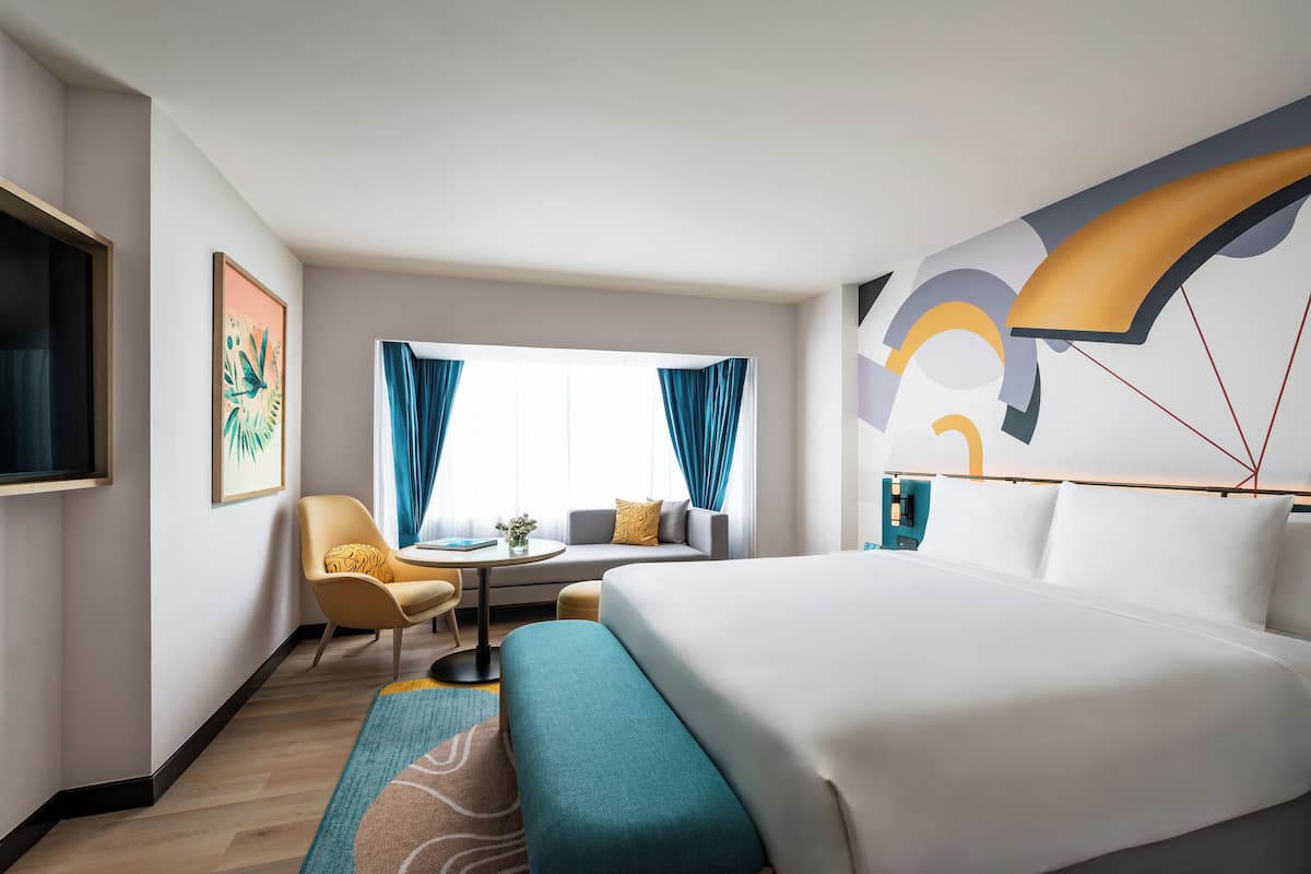 A hotel room with a bed, a sofa, a chair, a small table, and a TV.