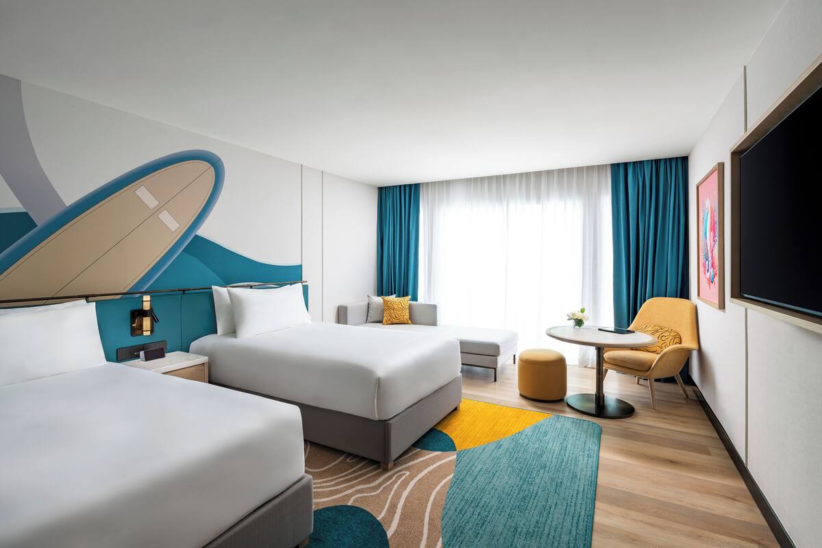 A hotel room with two beds, a sofa, a small table, and a TV.