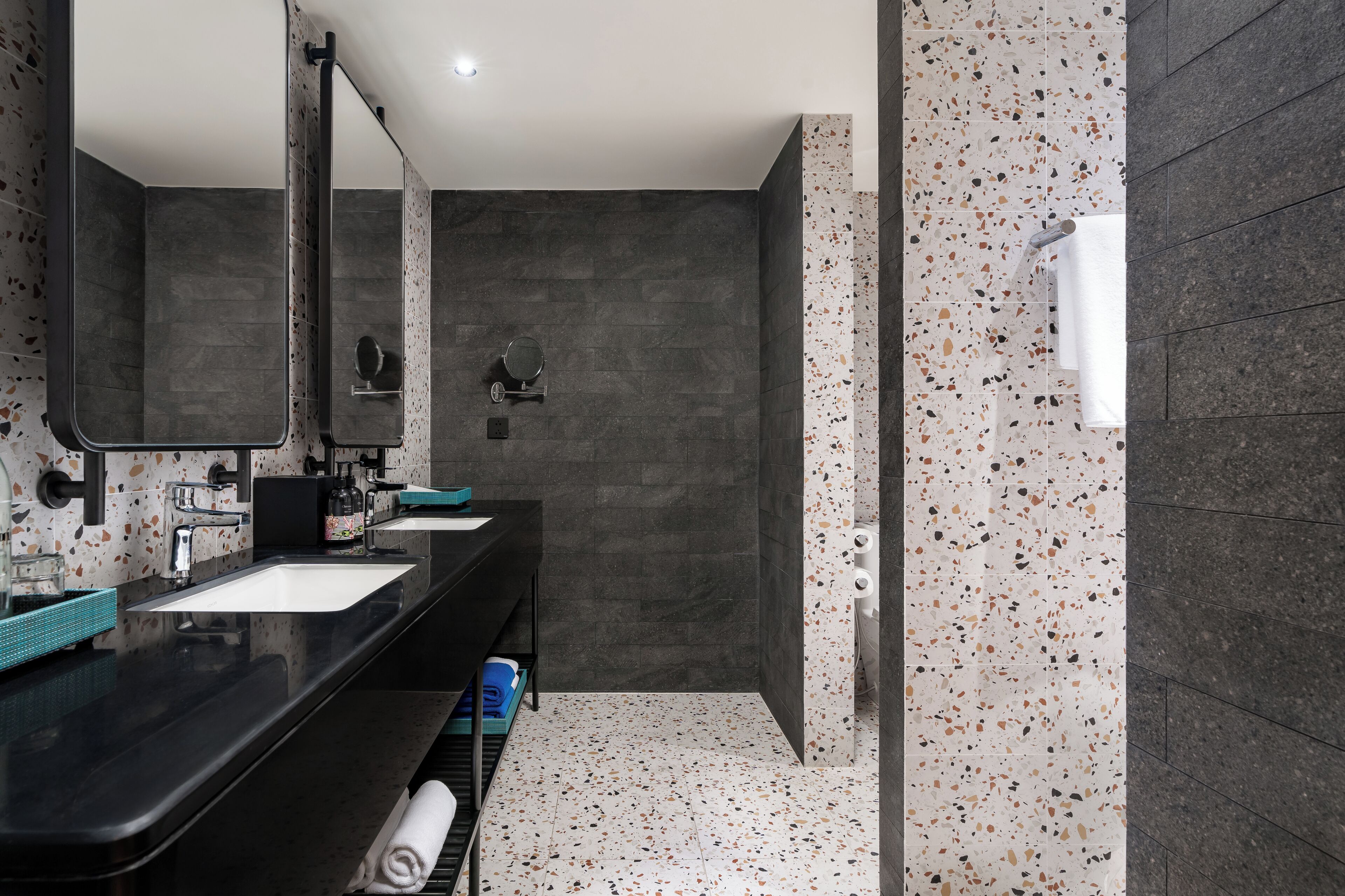 A modern bathroom with dark tiles, a black countertop, and a large mirror.
