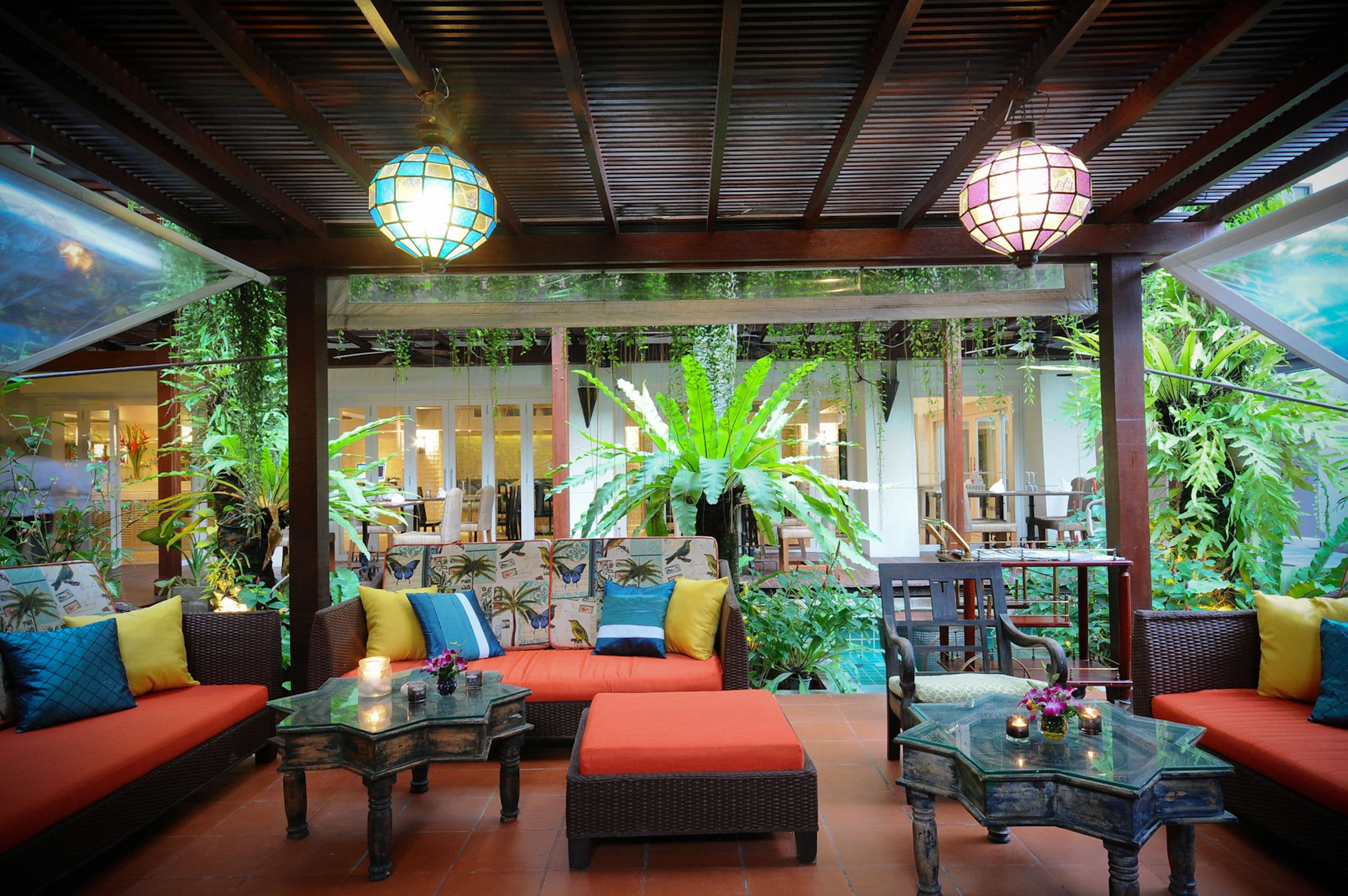 Un jardí interior amb mobles de vimetla, una taula de cafè de vidre i plantes penjants.