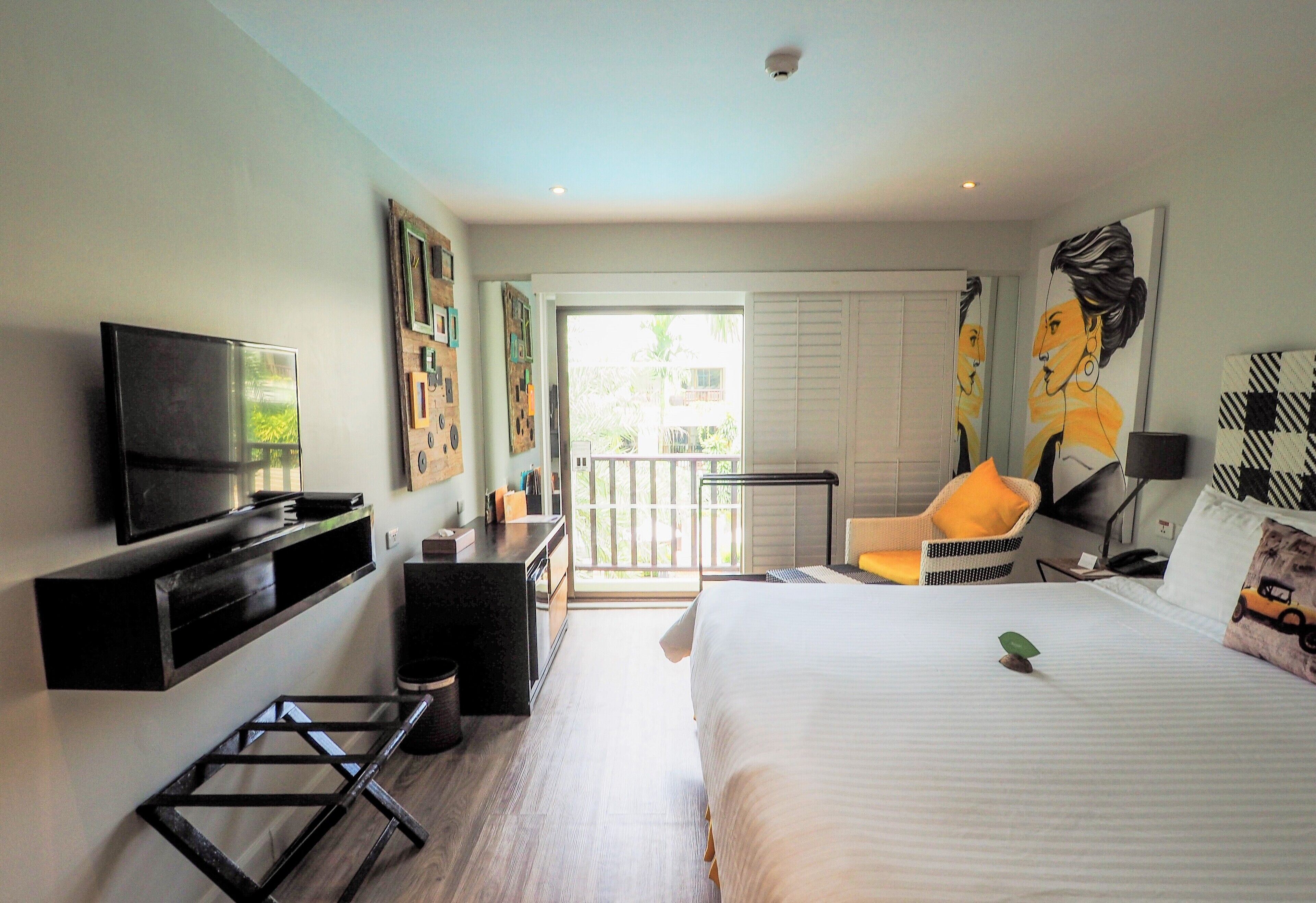 A hotel room with a bed, a TV, a desk, a chair, and a balcony with a view of the outside.