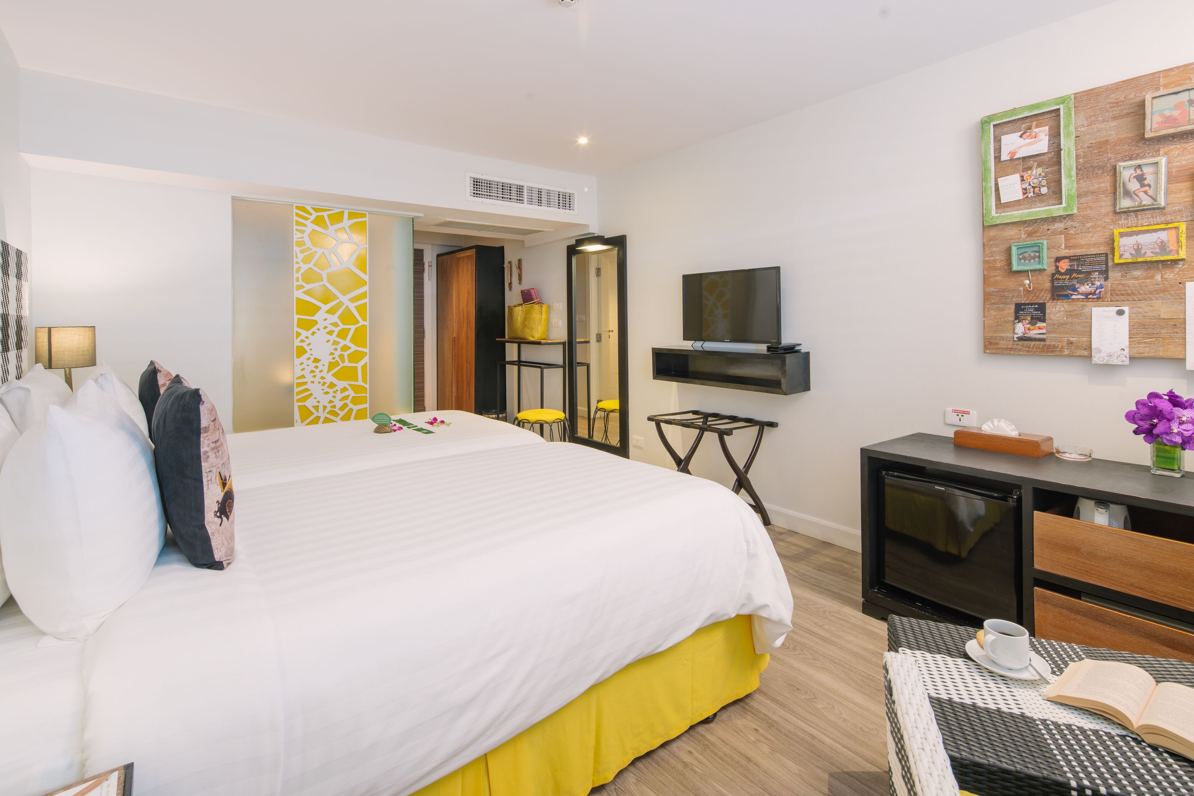 A hotel room with a large bed, a desk with a television, a mirror, and a bulletin board with pictures.