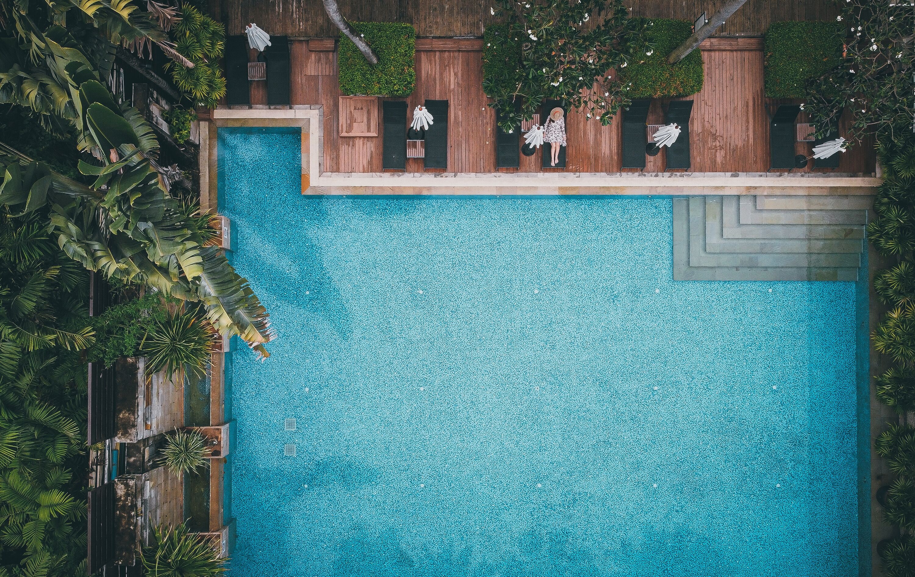 An aerial view of a swimming pool surrounded by lush greenery and wooden structures.