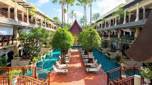 Ein Hotel mit zentral gelegener Poolanlage, umgeben von üppiger Vegetation und Palmen.