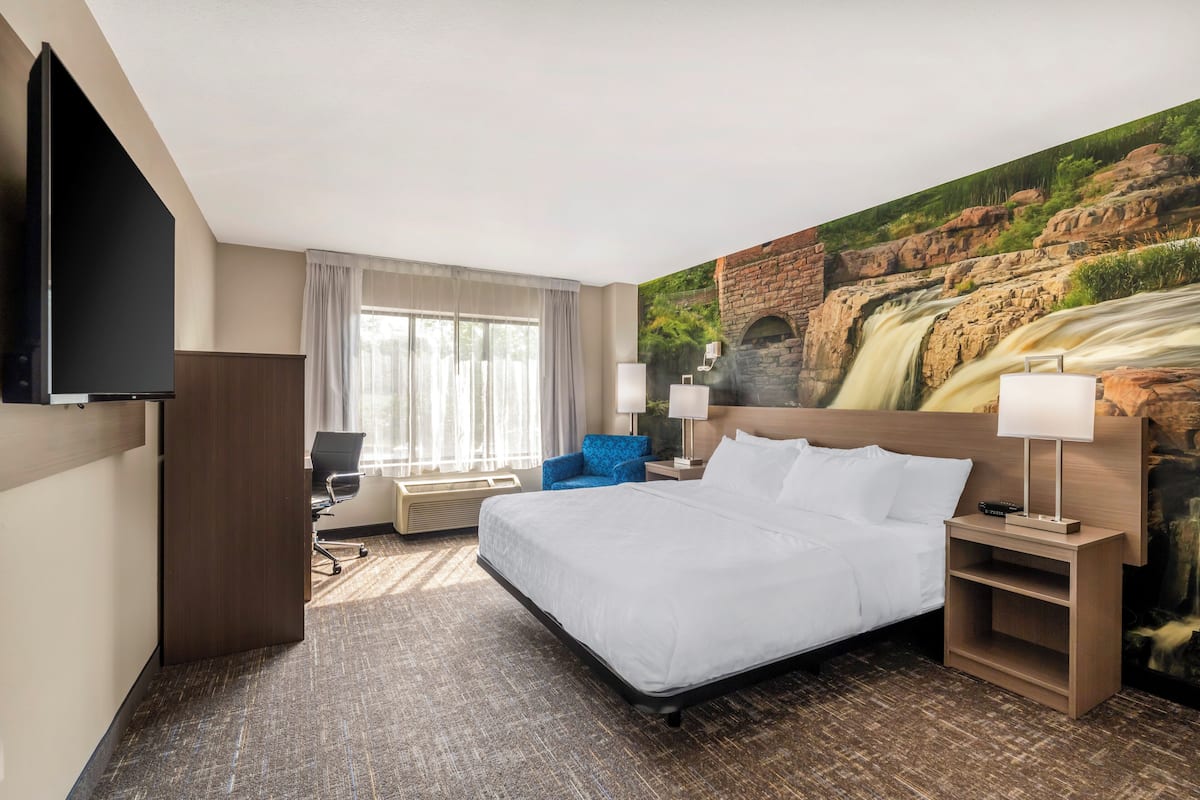 Ein Hotelzimmer mit einem großen Bett, einem Schreibtisch, einem Stuhl, einem Fernseher und einem Wandbild mit einem Wasserfall.