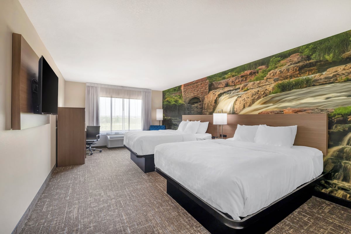 Ein Hotelzimmer mit zwei Betten, einem Fernseher, einem Schreibtisch und einem großen Wandbild eines Wasserfalls.