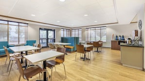 A spacious indoor area with tables and chairs, large windows, and a kitchenette area. - Clarion Pointe Sioux Falls Airport (Sioux Falls)