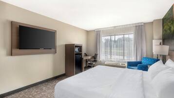 Una habitación de hotel con una cama grande, un escritorio con computadora, un televisor montado en la pared y una ventana con cortinas.