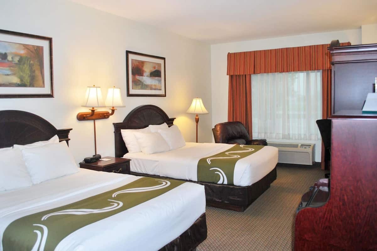 Ein Hotelzimmer mit zwei Betten, einem Schreibtisch, einem Sessel, einem Fernseher und einem Fenster mit Vorhängen.