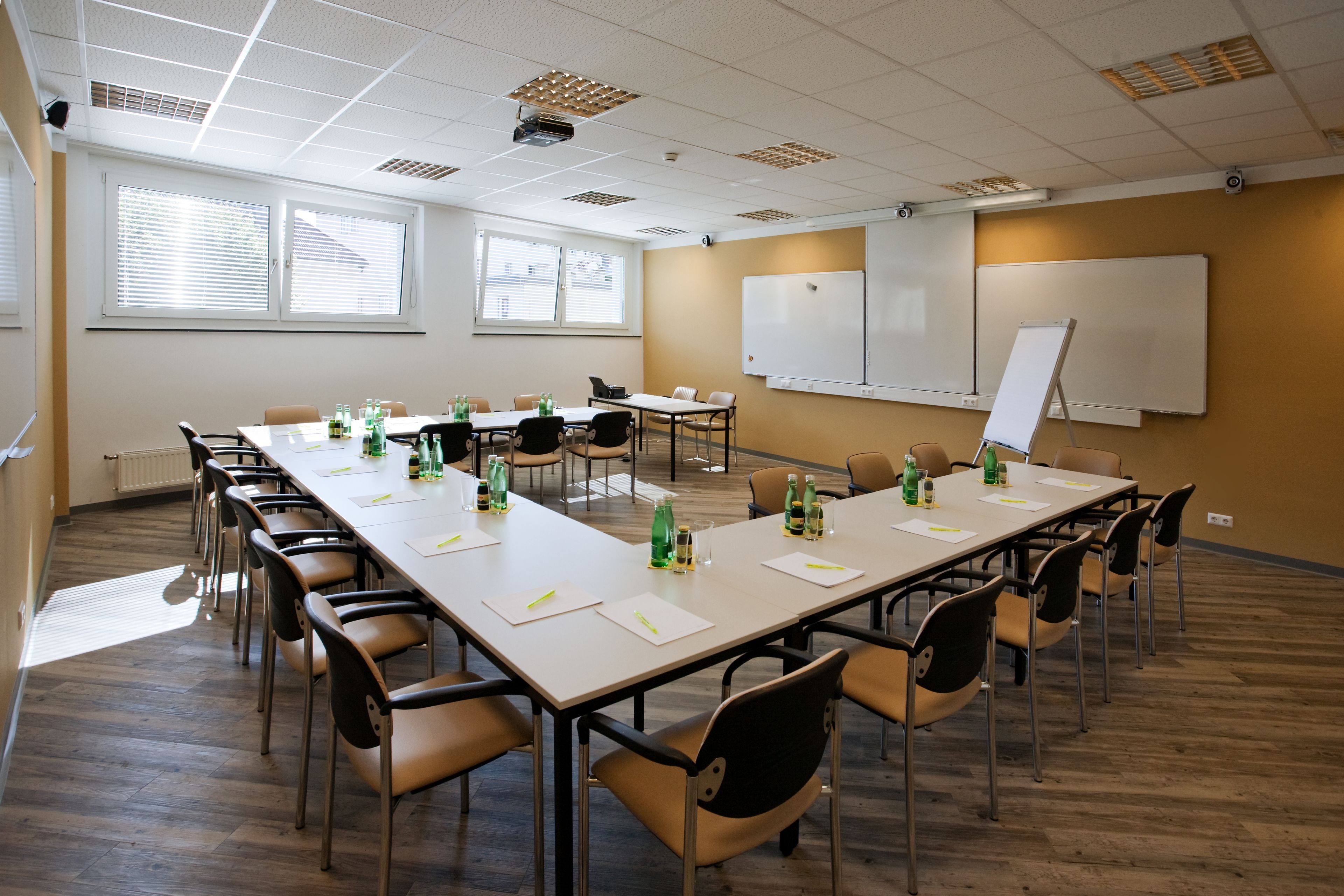 A conference room with a long table, chairs, a whiteboard, and windows with blinds.