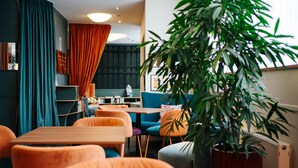 A modern hotel room with a dining area, a large plant, and a blue sofa. - Hotel City Villach (Villach)