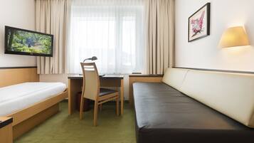 A hotel room with a bed, a desk, a chair, a TV, and a sofa.