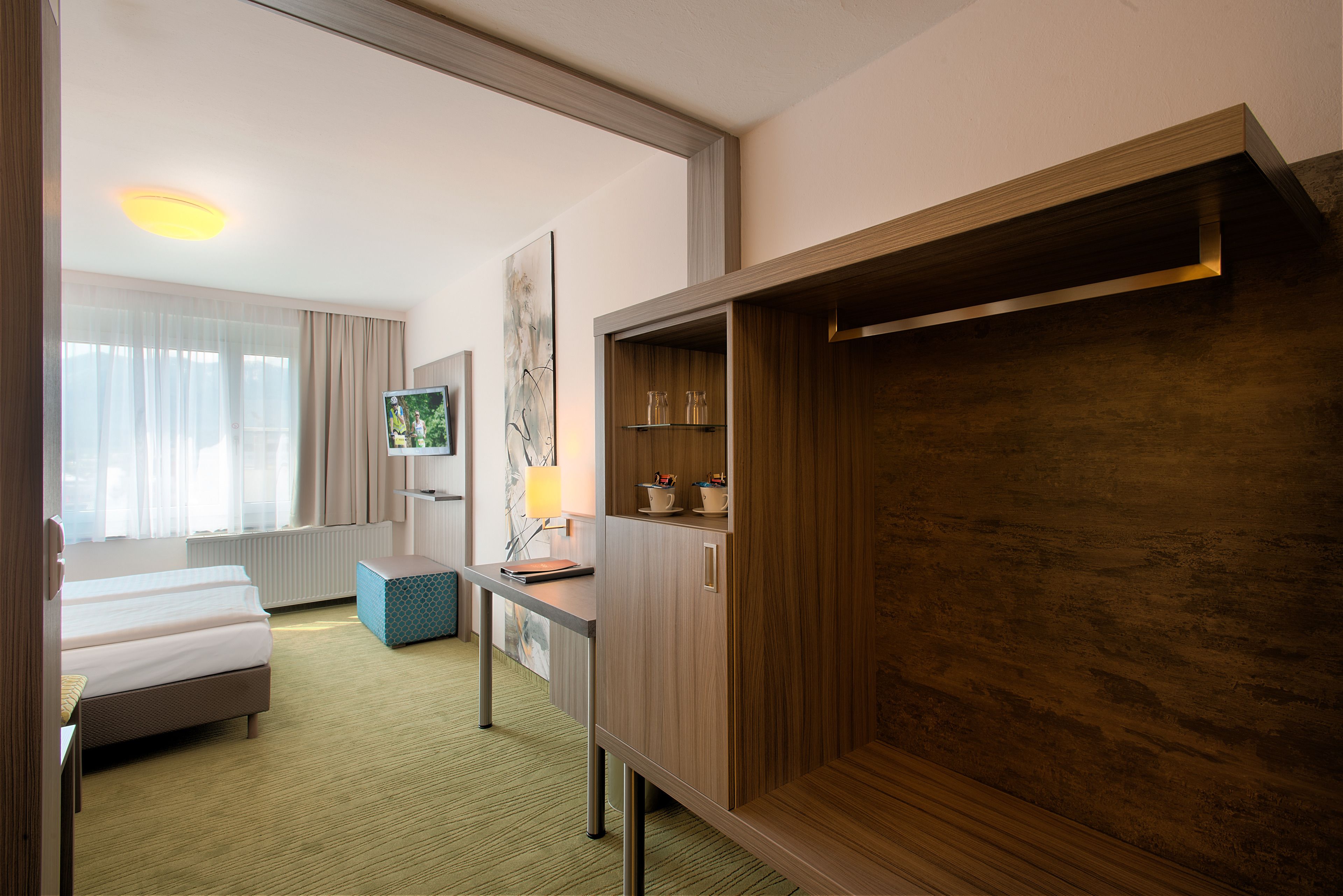 A hotel room with a bed, a desk, a wardrobe, and a television.