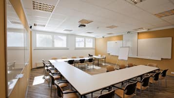 A conference room with a long table, chairs, whiteboards, and windows with blinds.