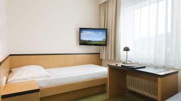A hotel room with a single bed, a desk, a television mounted on the wall, and a window with curtains.