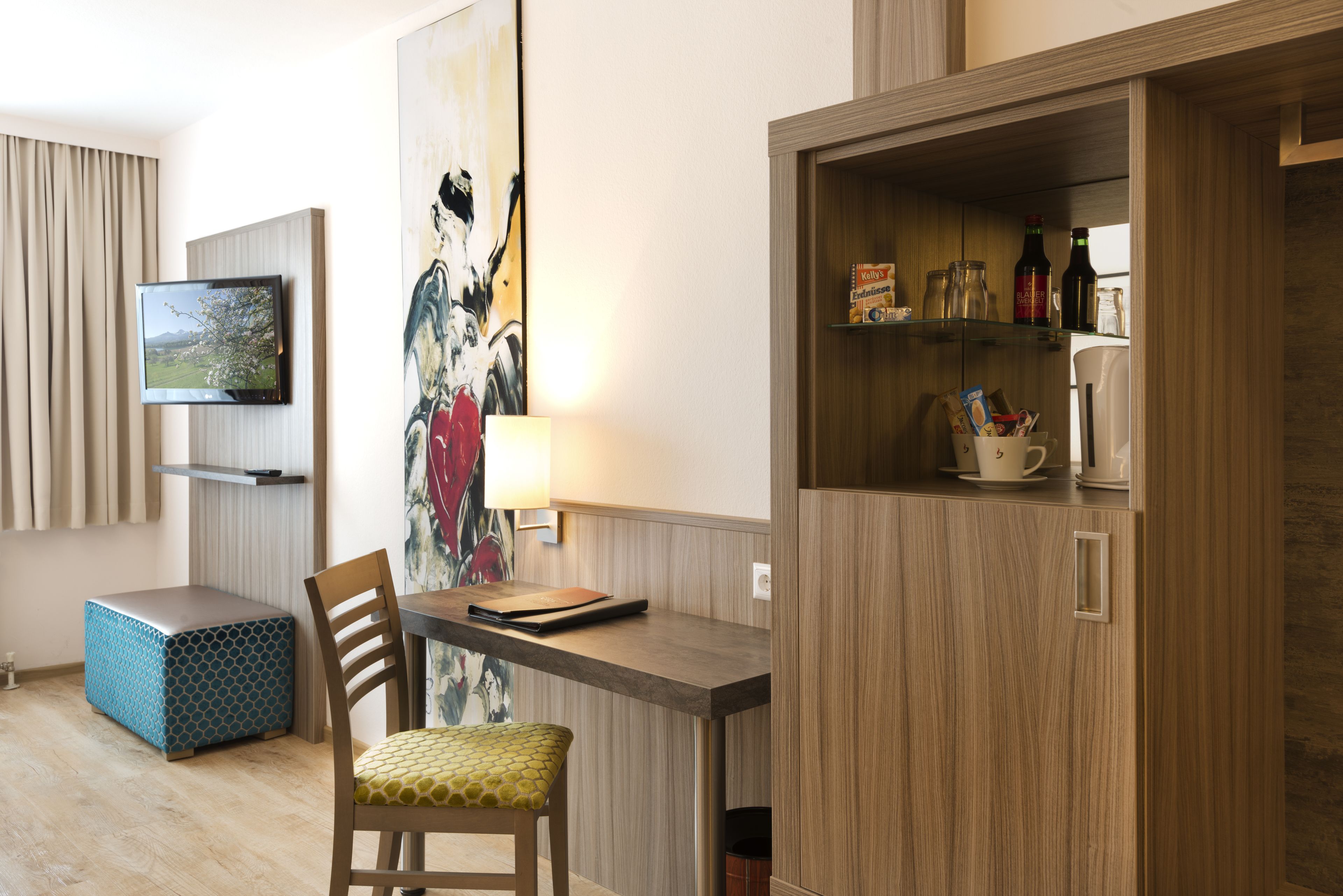 Una camera d'albergo moderna con un tavolo da pranzo in legno, una sedia comoda, un televisore montato a parete e un mobiletto con utensili da cucina.